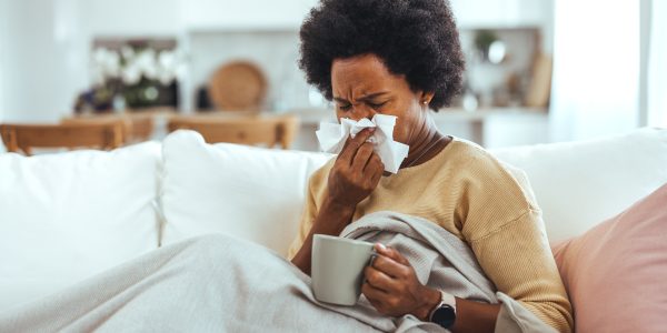 Person blowing nose with a lot of tissues and a cup of hot tea.
